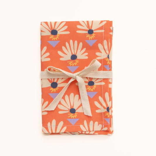 Orange red tea towel featuring a floral pattern wrapped in a ribbon on a white background.
