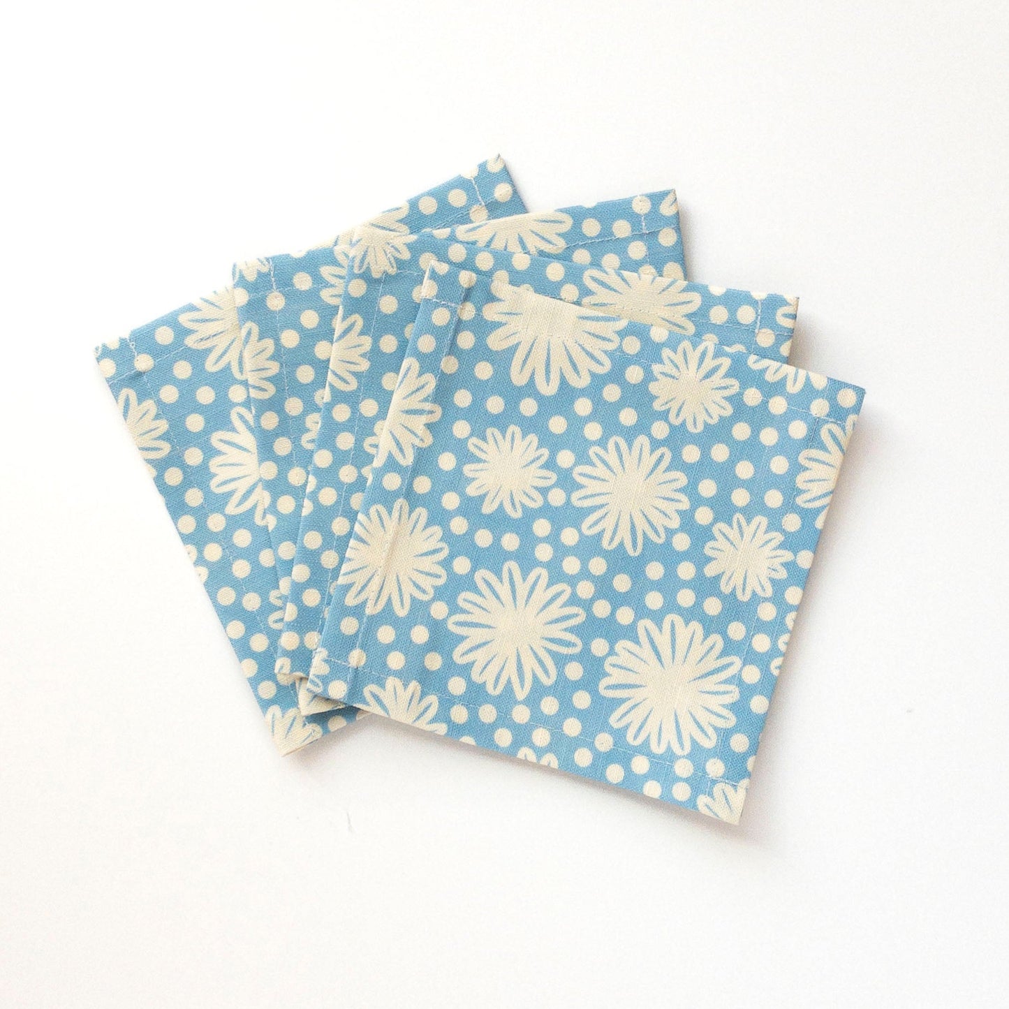 Four blue cocktail napkins with white floral patterns on a white background