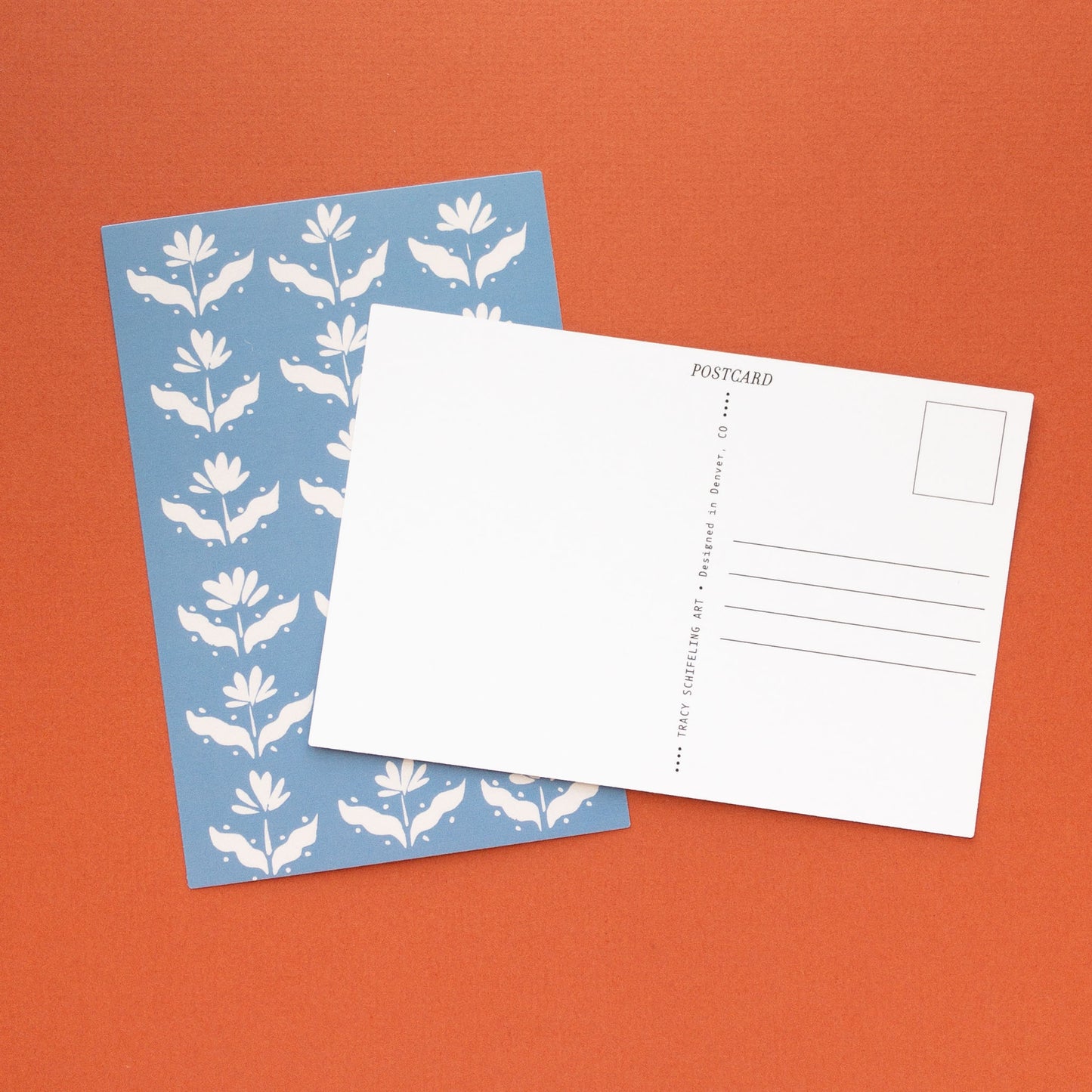 Blue and white floral postcard and a blank postcard back arranged on a red background.
