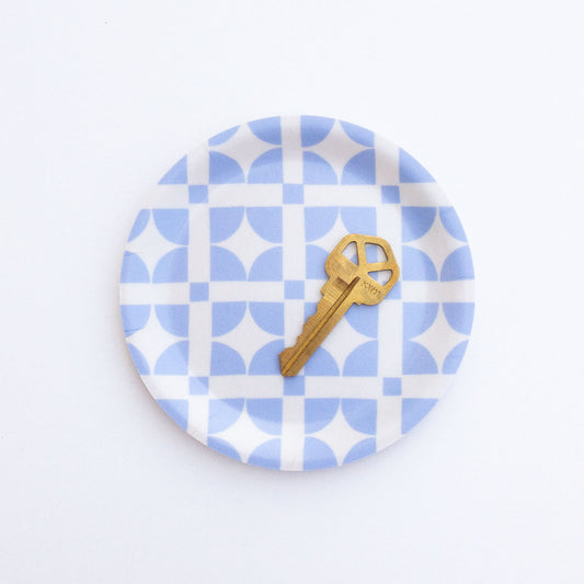 Round blue and white patterned coaster with a gold key on a white background