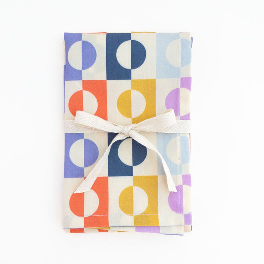 Colorful geometric tea towel folded and wrapped with a white ribbon on a white background.