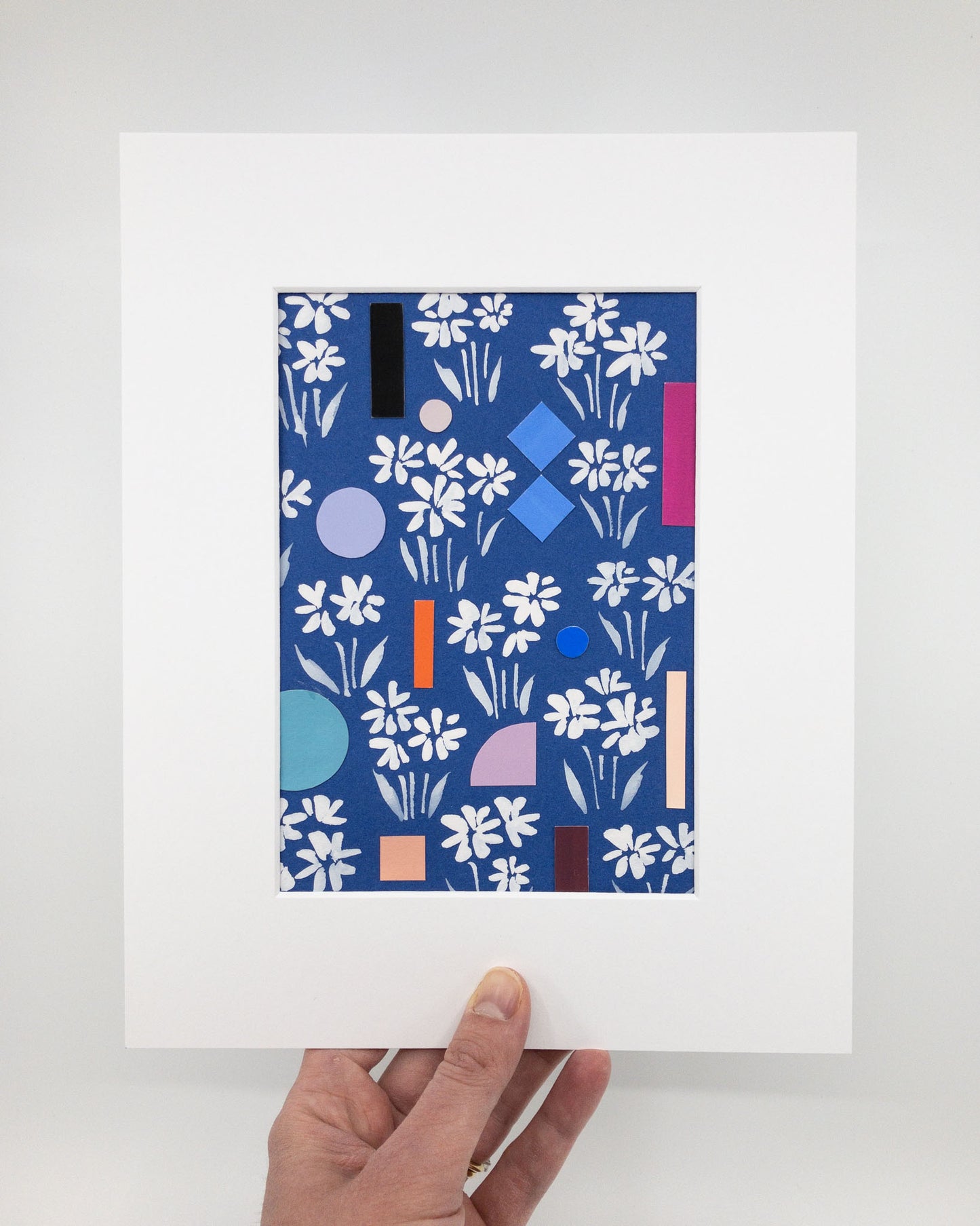 Hand-painted white flowers on a blue background interspersed with colorful geometric shapes. The artwork is in a white mat.