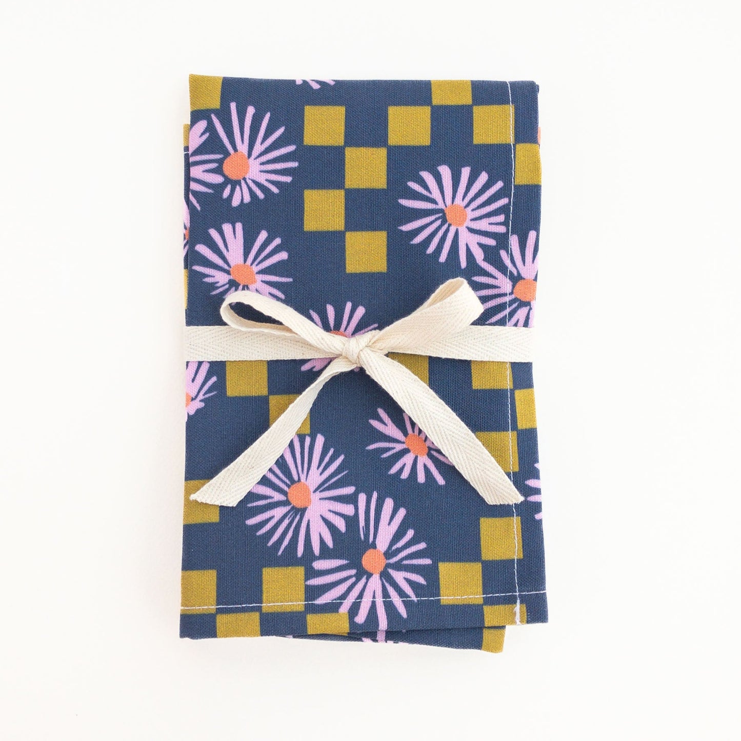 Folded tea towel with floral pattern and checkered design, tied with a white ribbon on a white background.