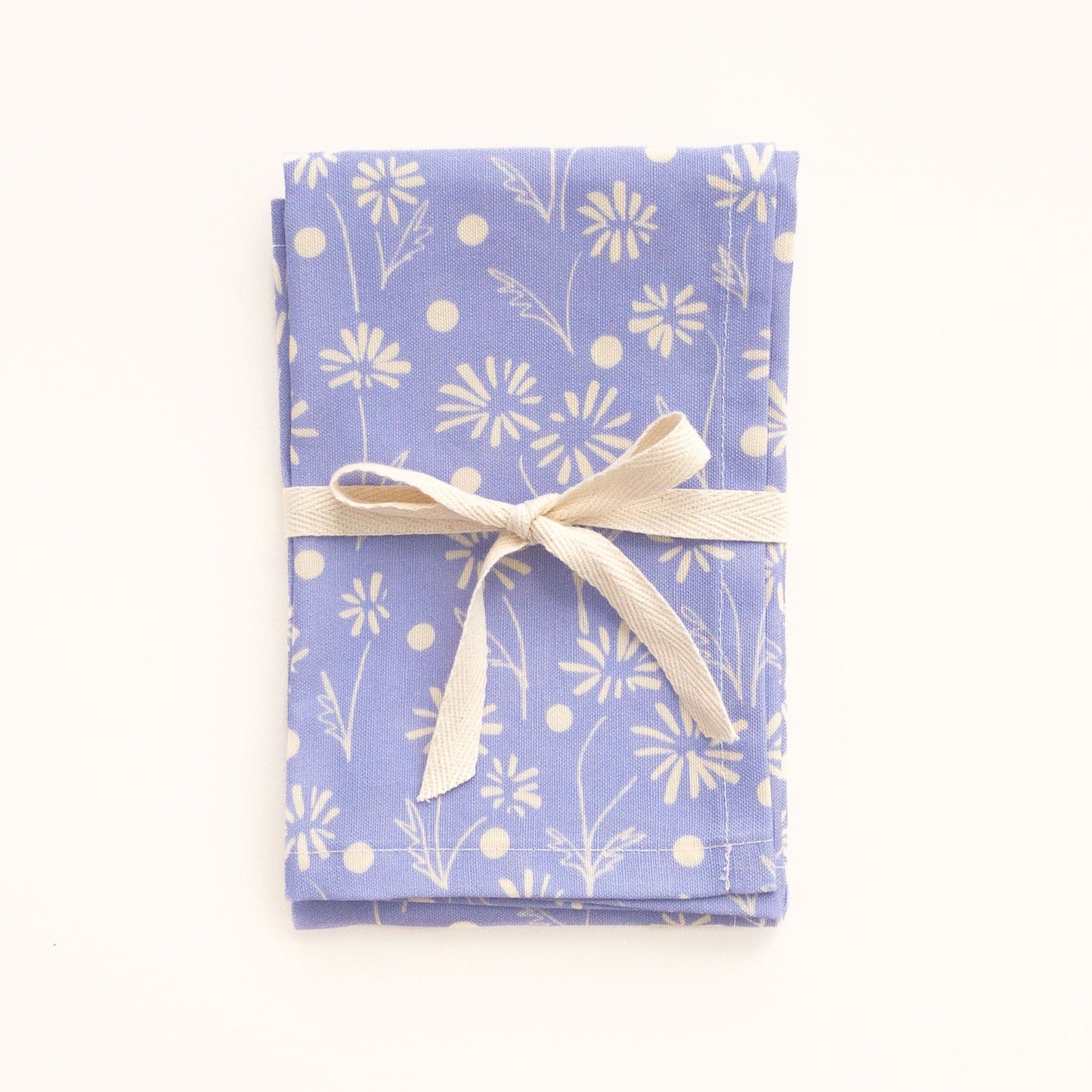 Folded periwinkle blue tea towel with a white floral pattern tied with a ribbon on a white background.