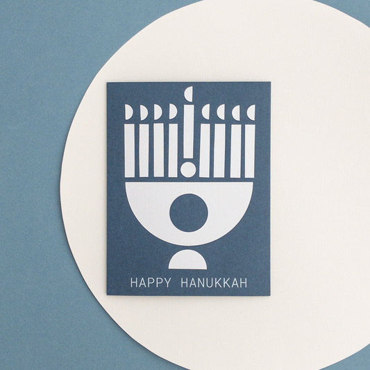 Happy Hanukkah card with a blue background and white menorah design on a blue and white circular background.