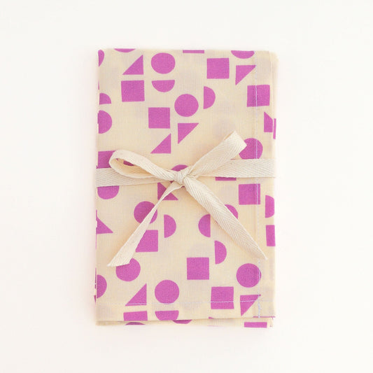Tea towel featuring a pink geometric pattern design tied with a white ribbon on a white background.