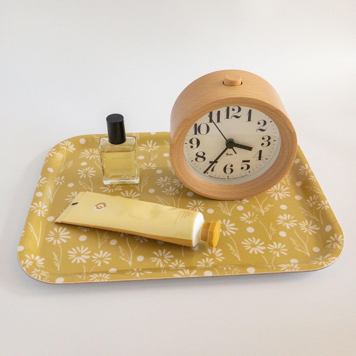Yellow daisy tray holding an alarm clock, perfume, and lotion tube on a white background.
