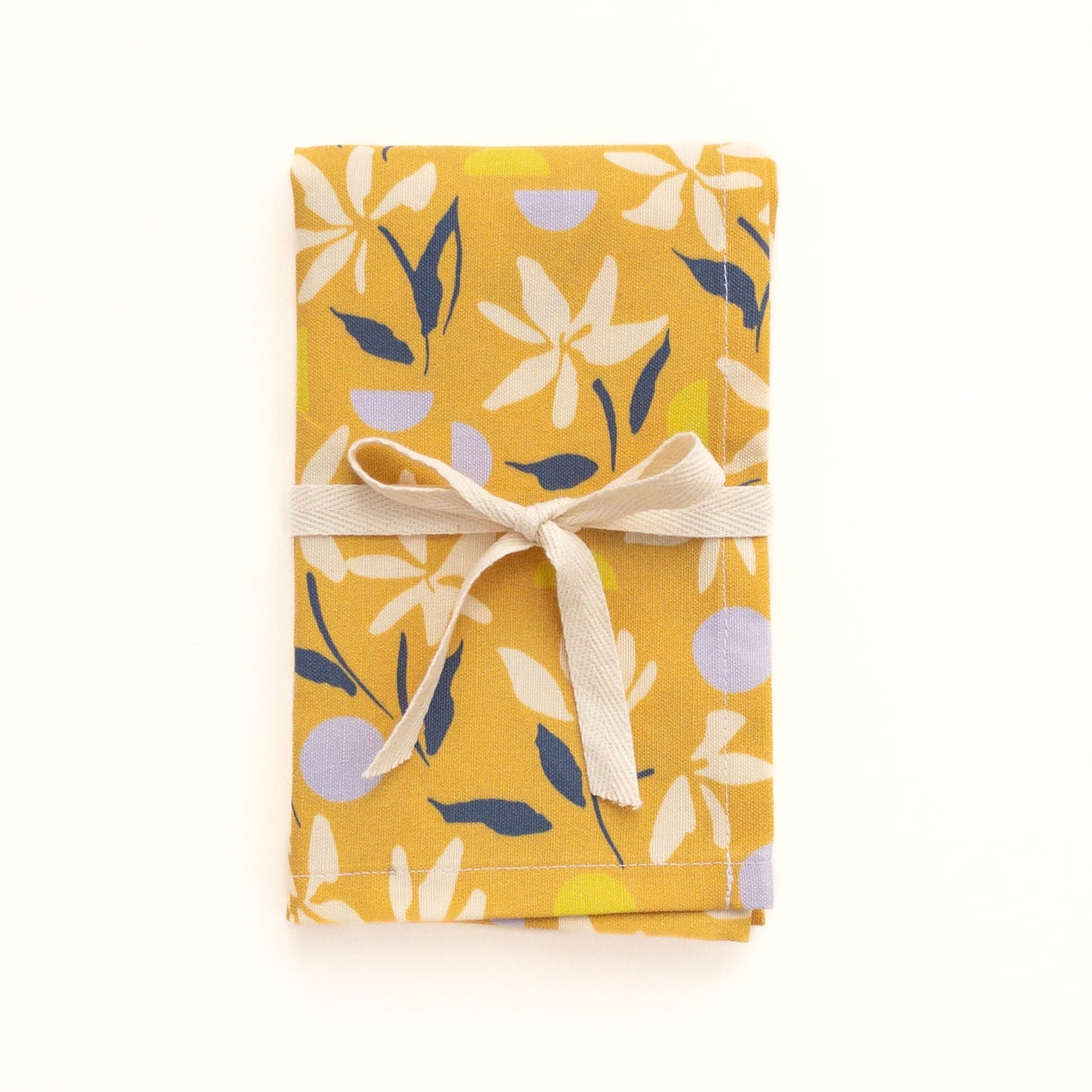 Folded yellow tea towel with floral design tied with a ribbon and a bow on a white background