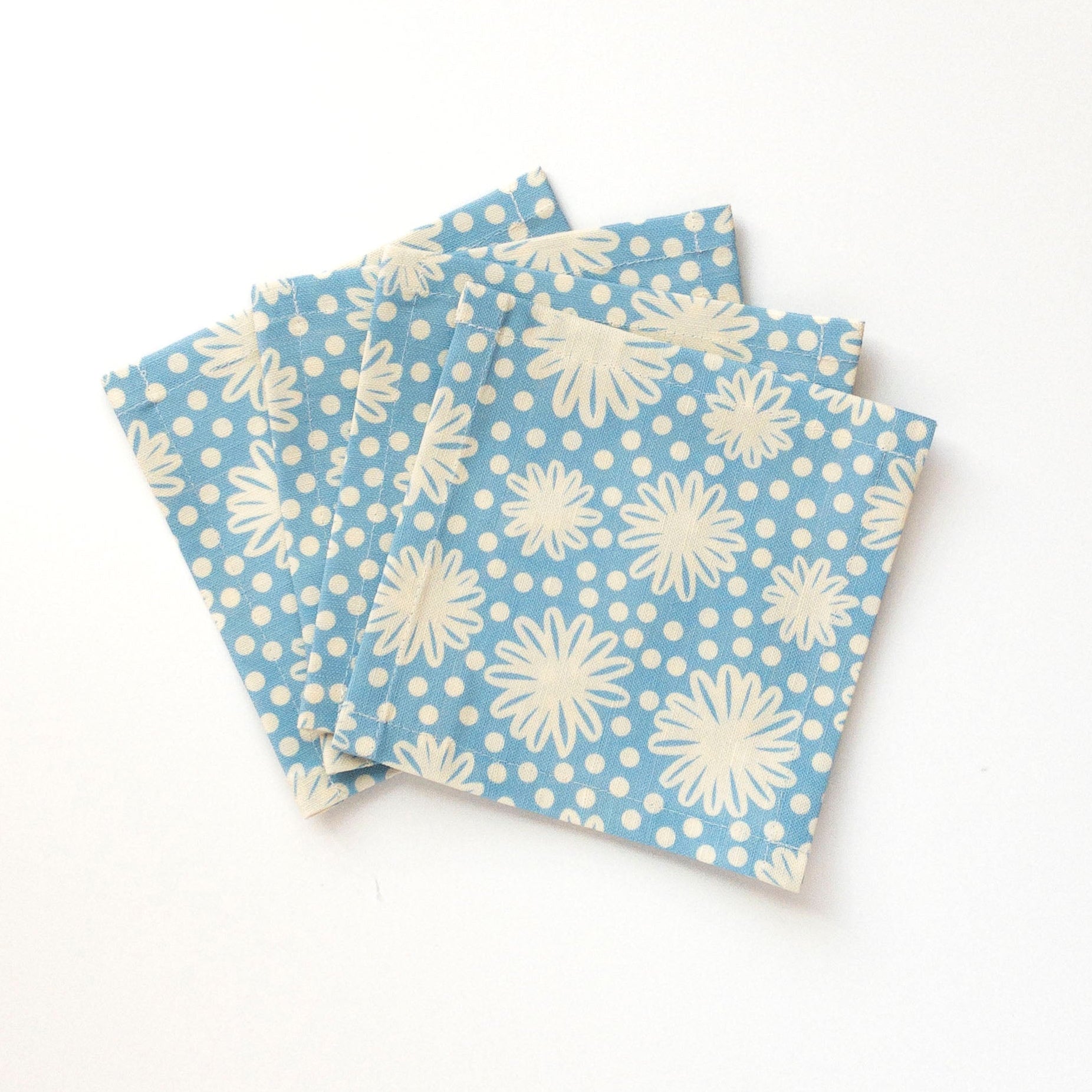 Four blue cocktail napkins with white floral patterns on a white background