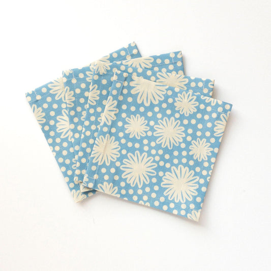 Four blue cocktail napkins with white floral patterns on a white background