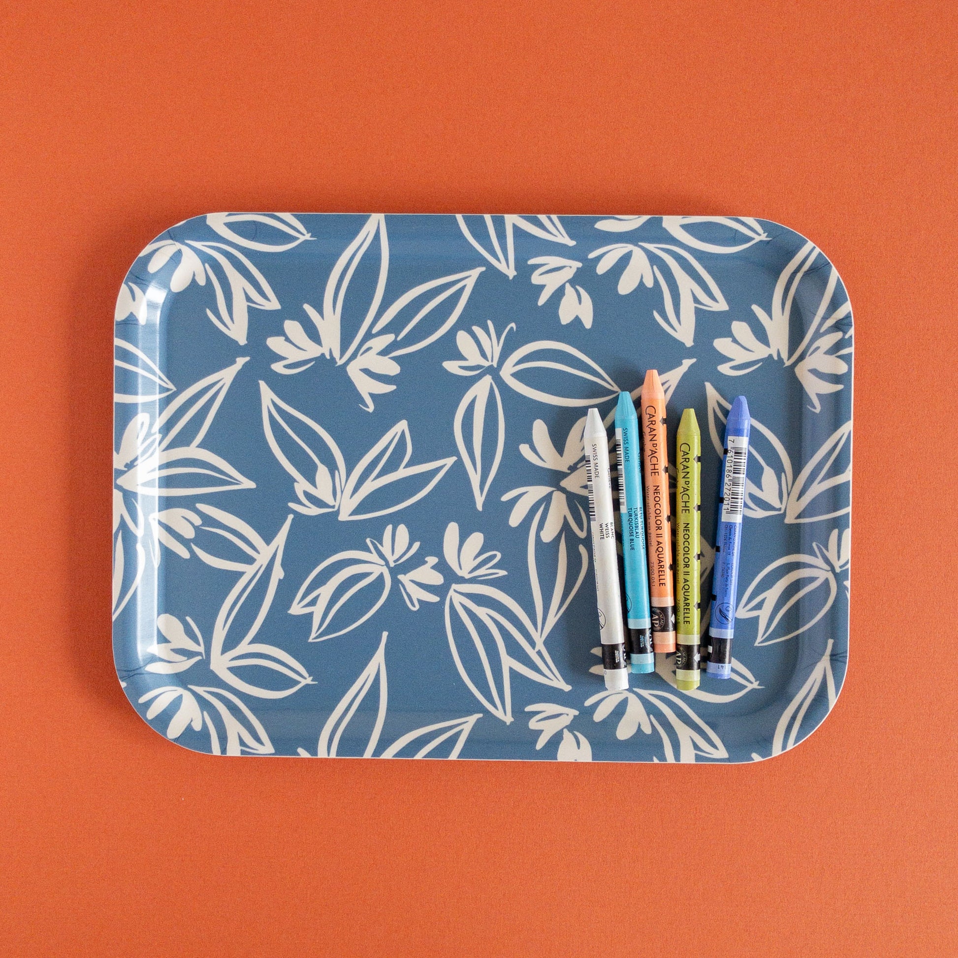 Blue floral tray holding five crayons on a red background.