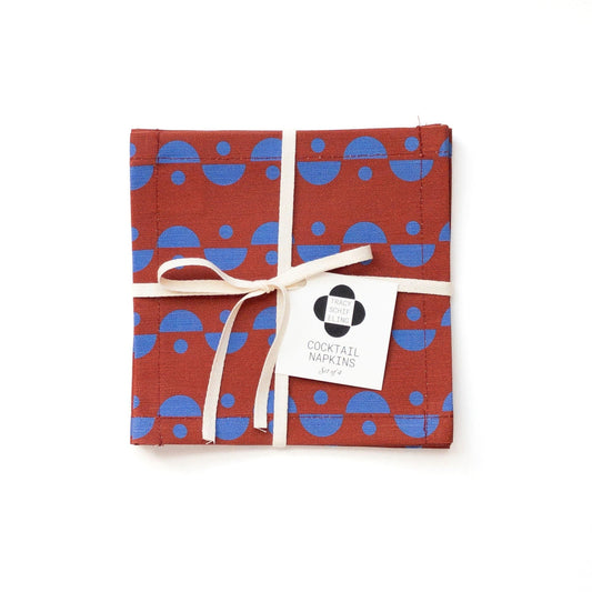 Set of cocktail napkins with blue geometric pattern on brown background, tied with a white ribbon.