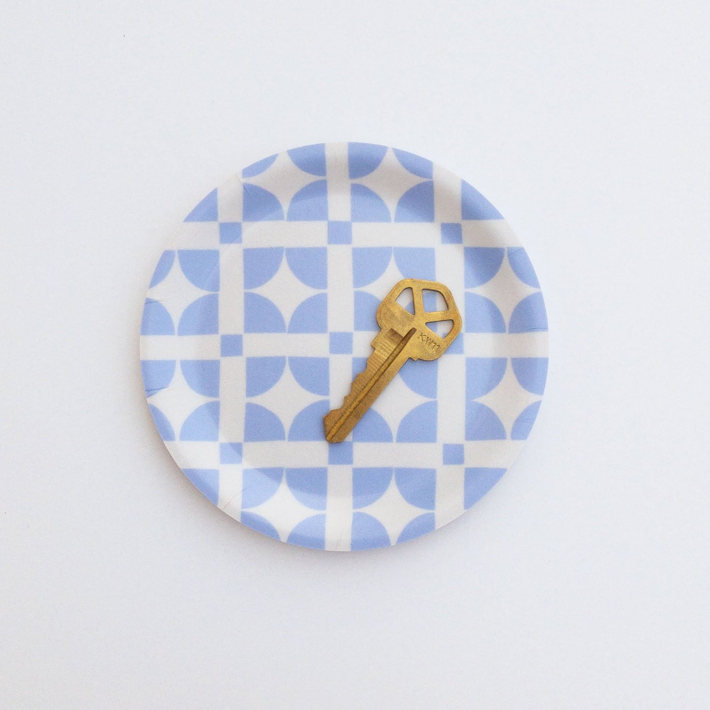 Round blue and white patterned coaster with a gold key on a white background