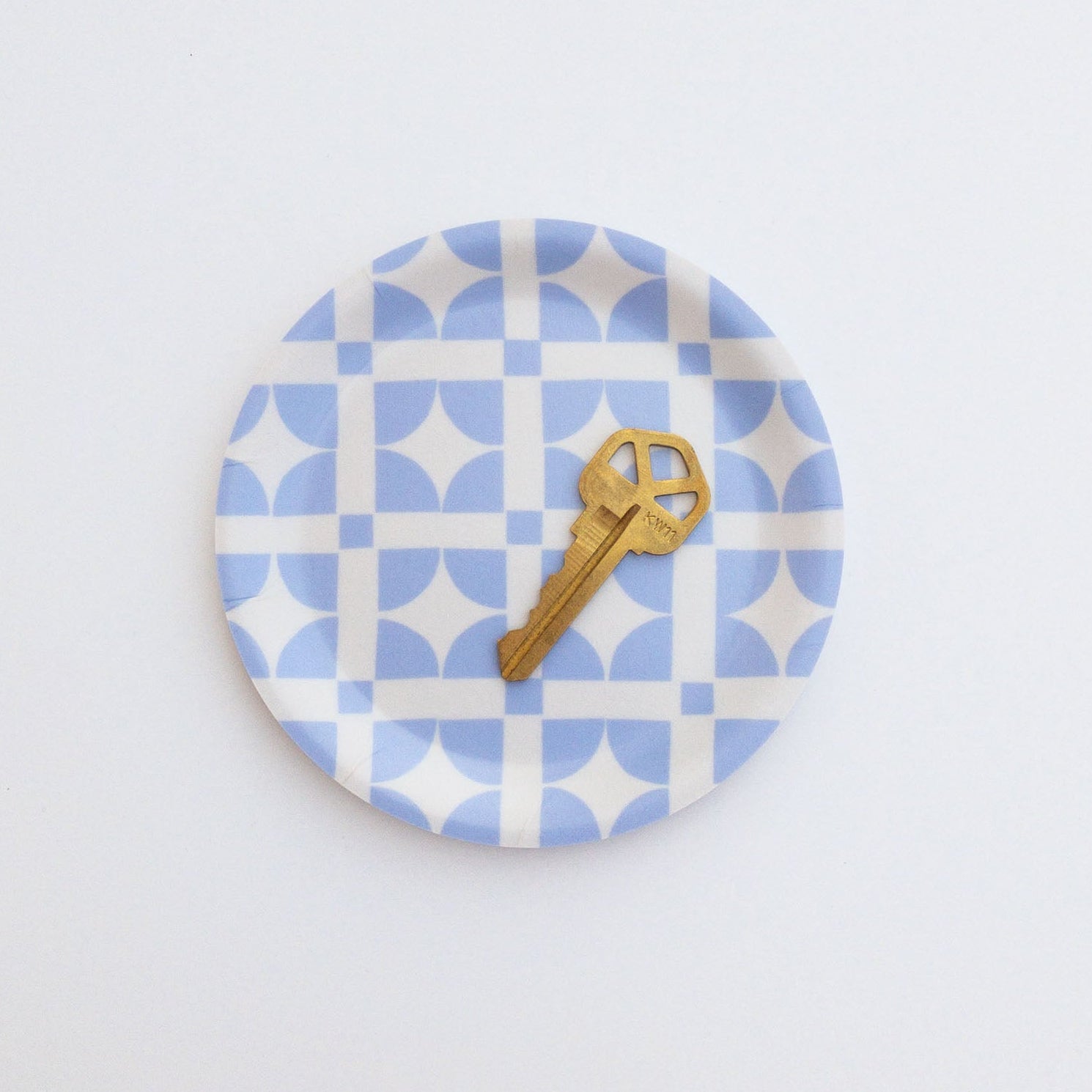 Round blue and white patterned coaster with a gold key on a white background