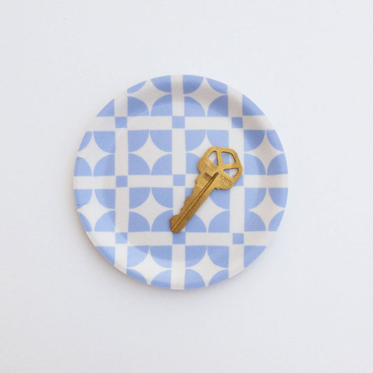 Round blue and white patterned coaster with a gold key on a white background