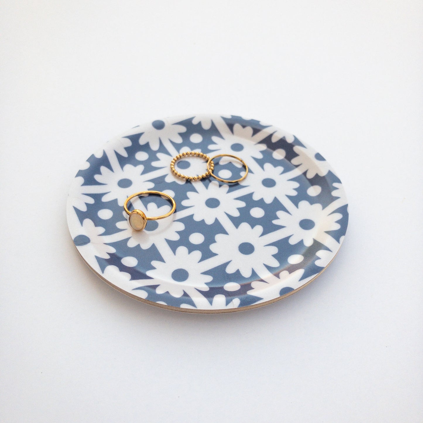 Round blue and white floral patterned coaster with gold rings on a white background