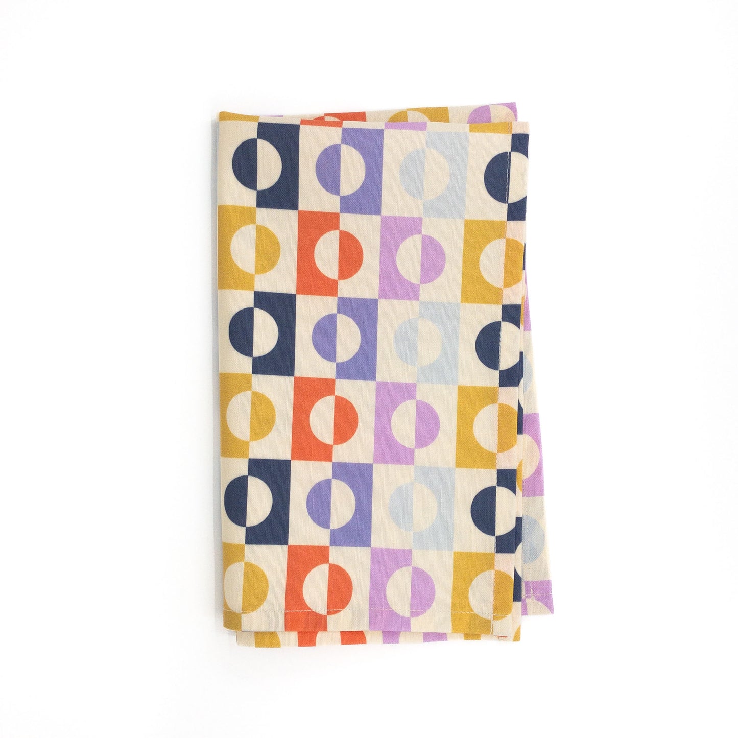 Folded tea towel with a colorful geometric pattern of circles and squares on a white background.