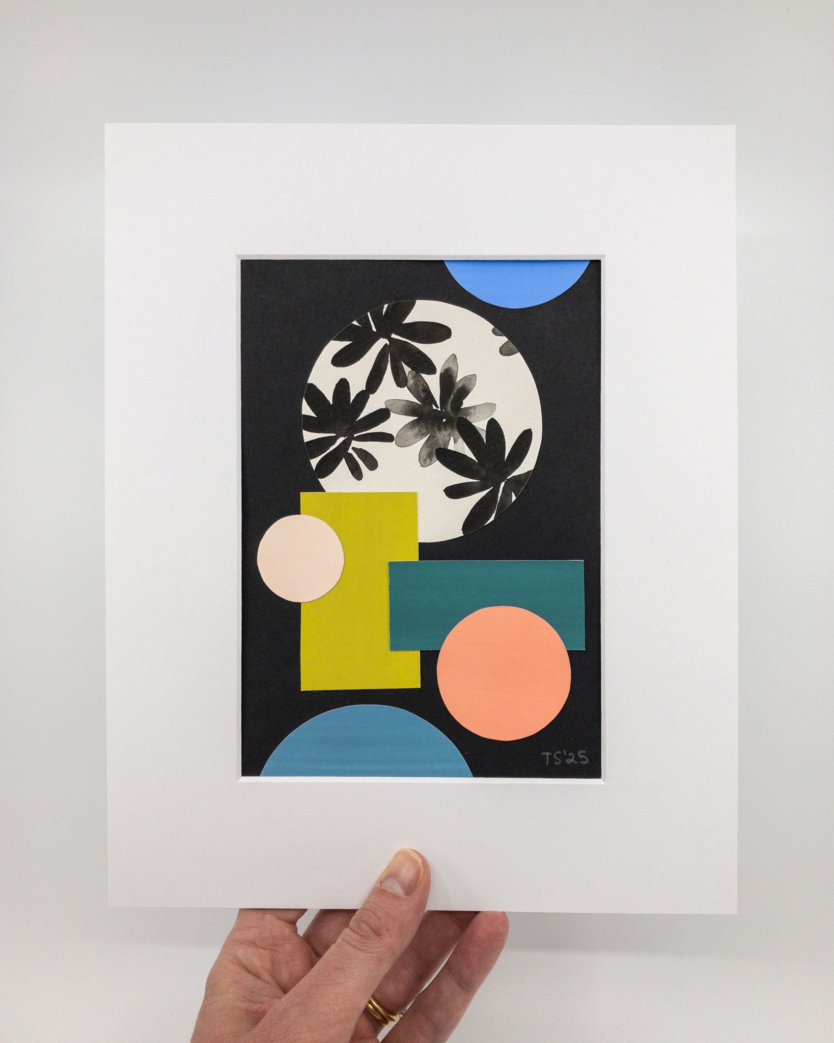 Colorful geometric collage featuring circles and rectangles in pinks, blues, and greens. The largest central circle shape has hand-painted florals. The background is black, and the artwork is mounted in a white mat.