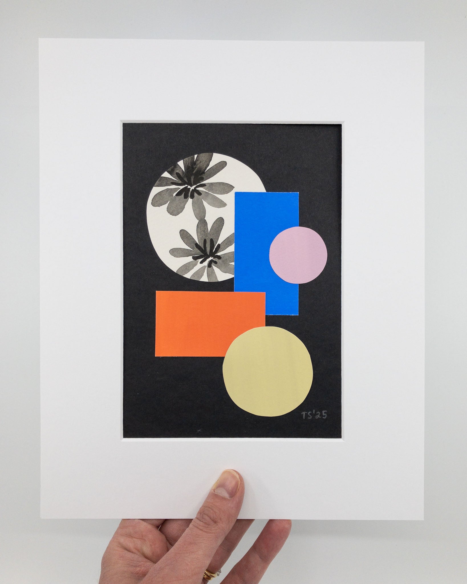 Colorful geometric collage on black background. The artwork features red, blue, yellow, and purple shapes and a hand-painted black and white floral. The artwork is in a white mat.