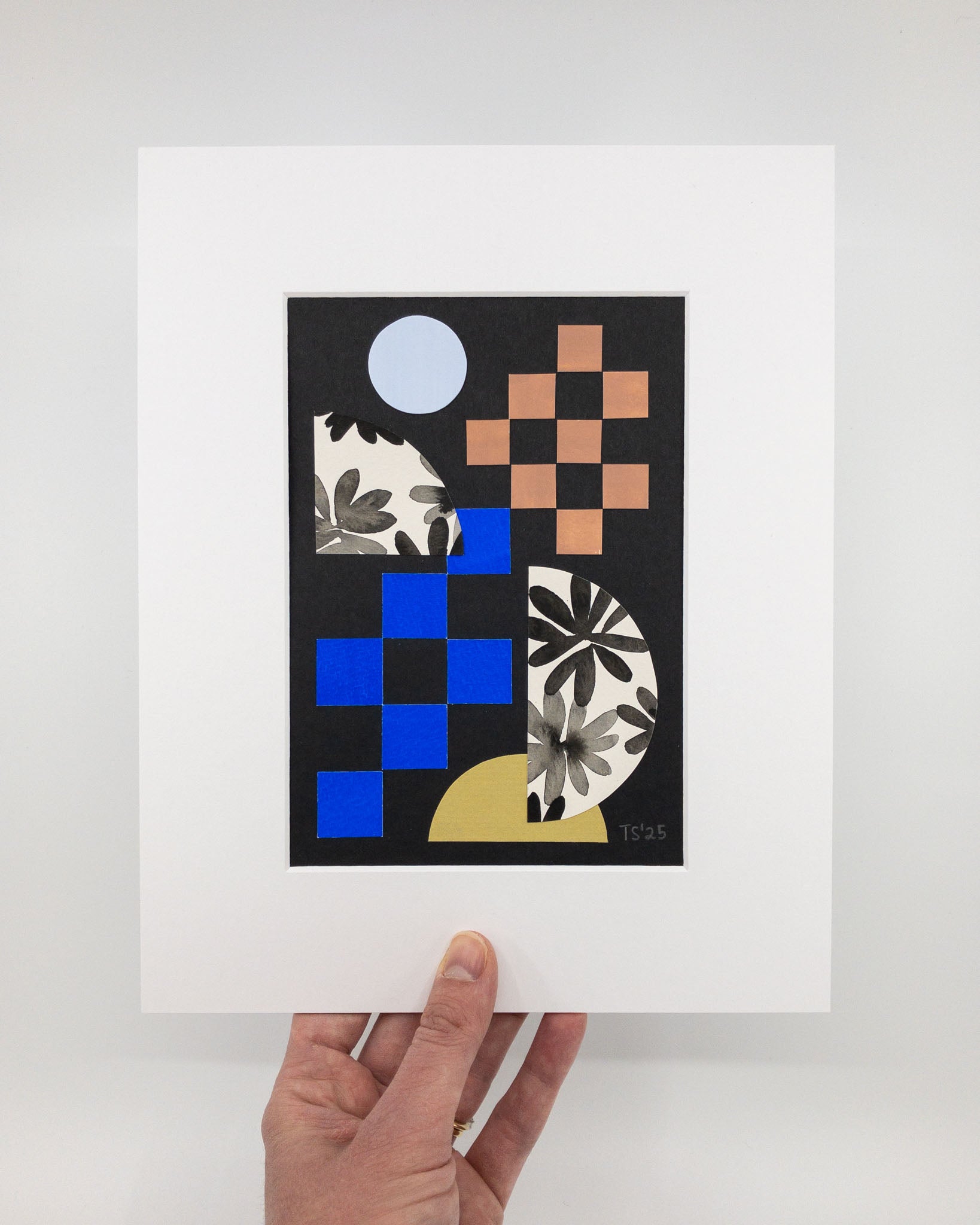 Original artwork featuring blue and brown squares and circle shapes with floral motifs on a black background. The artwork is in a white mat.