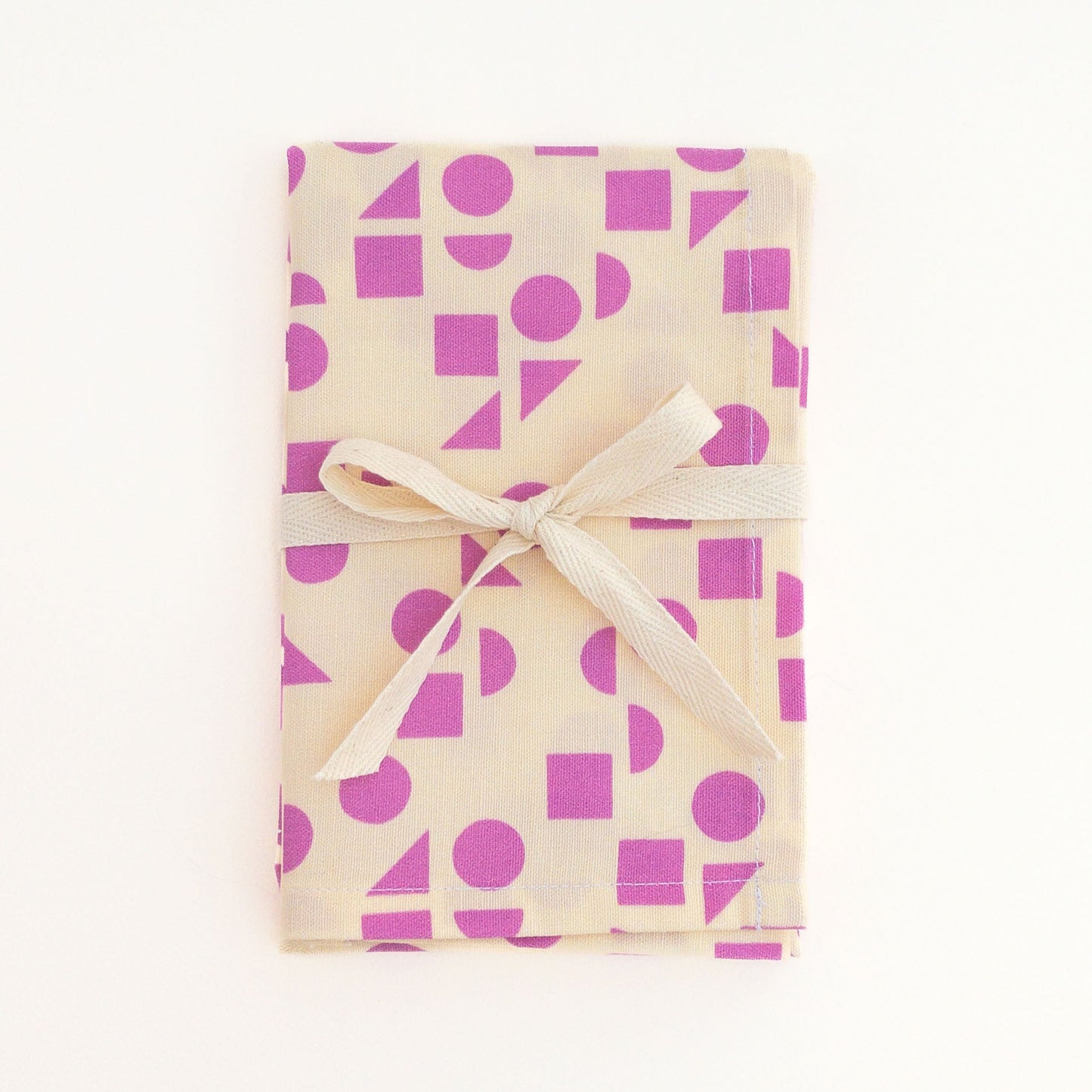 Tea towel featuring a pink geometric pattern design tied with a white ribbon on a white background.