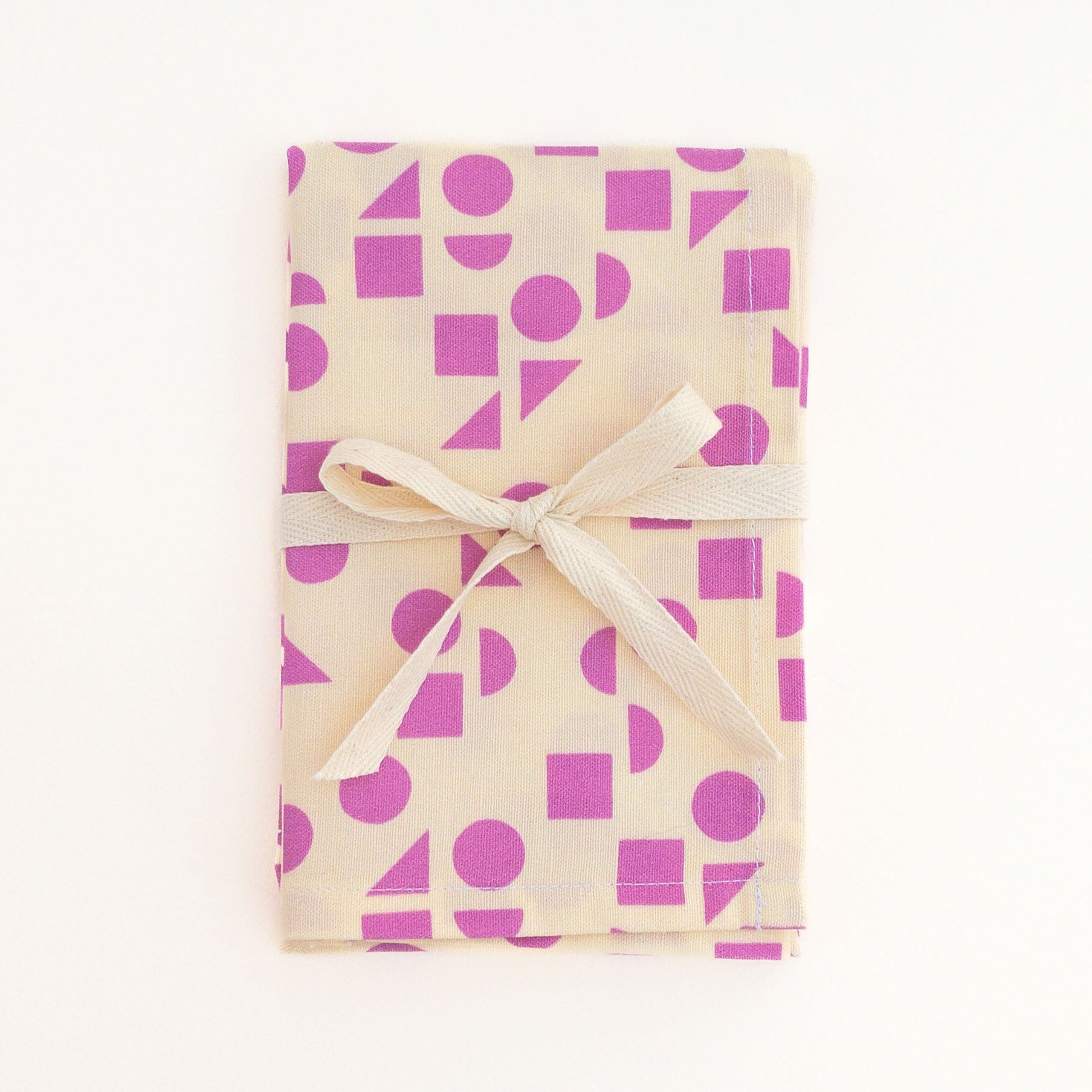 Tea towel featuring a pink geometric pattern design tied with a white ribbon on a white background.