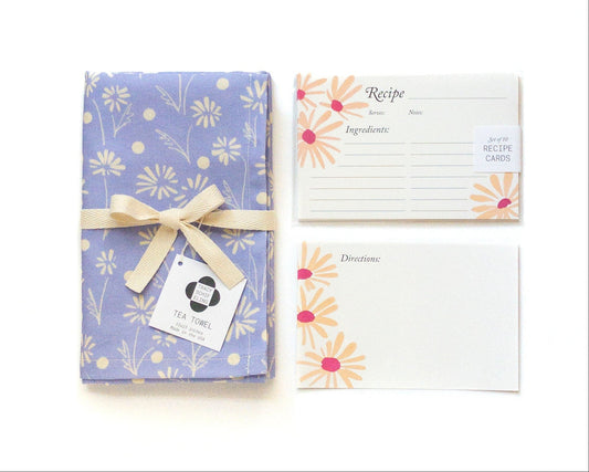 Floral-patterned tea towel with a bow, accompanied by recipe cards on a white background
