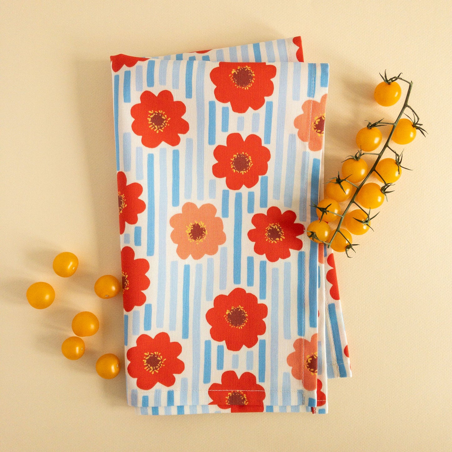 Folded tea towel with a floral and stripe pattern, styled with small yellow tomatoes.